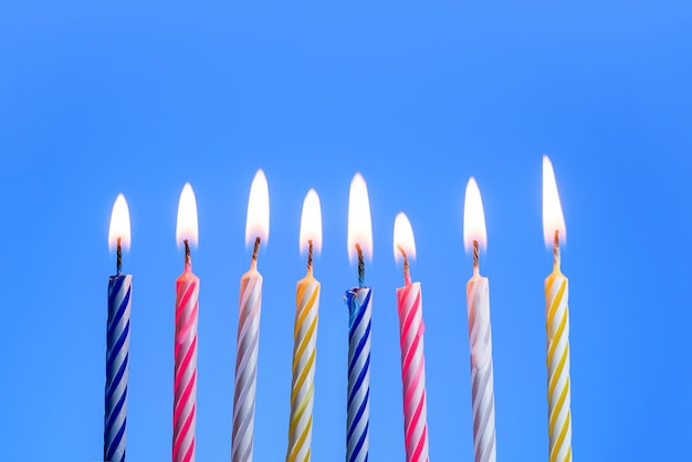 Eight burning candles for a birthday cake on a blue background with copy space.