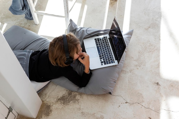 Eight year old boy lying on cushions chin on hands watching a
laptop screen doing homework