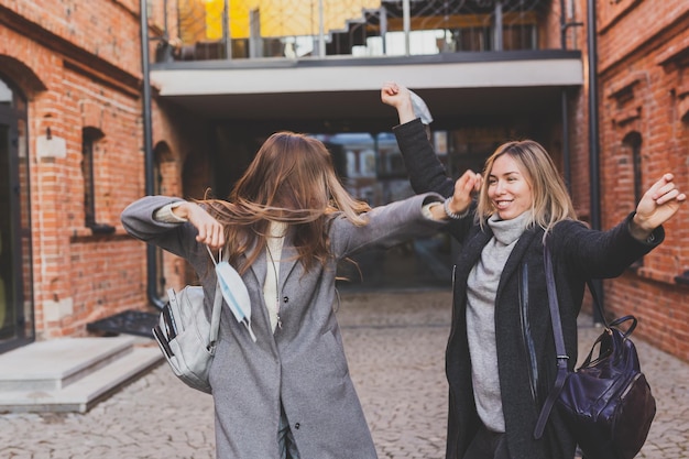 Einde van de pandemie van het coronavirus, gelukkige vrouwen die medische maskers afzetten, dansen en voelen in stadsvrouwen