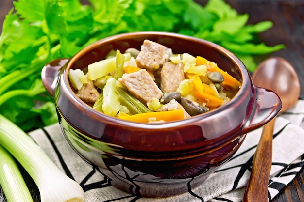 Photo eintopf soup made from pork, celery, beans, carrots and potatoes with leek in a clay bowl on a napkin on wooden board background