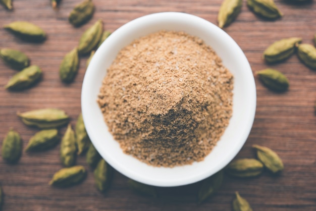 Elaichi or Cardamom powder in bowl or heap over moody background with pods. selective focus