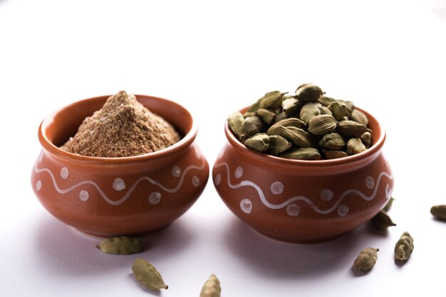 Elaichi or Cardamom powder in bowl or heap over moody background with pods. selective focus