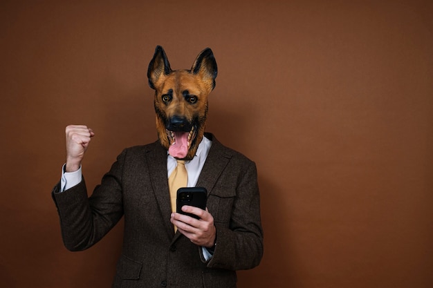 Un uomo euforico con smartphone e una maschera per la testa di cane in lattice che alza le mani