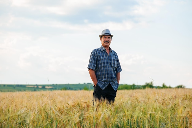 Foto anziano nell'agricoltura l'agricoltore anziano sta in piedi con le mani in tasca indossando un cappello