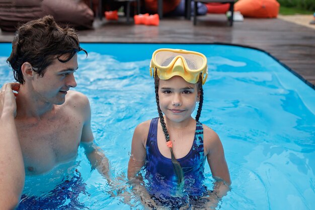 Elder brother training little sibling to swim in swimming pool outdoor at summer healthy lifestyle