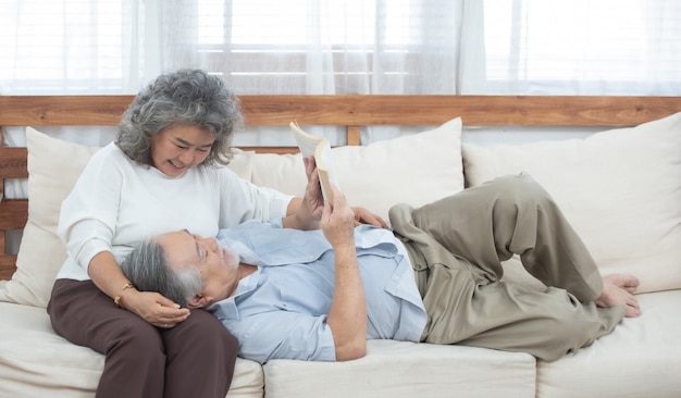 Elder couple sit on couch read book at home