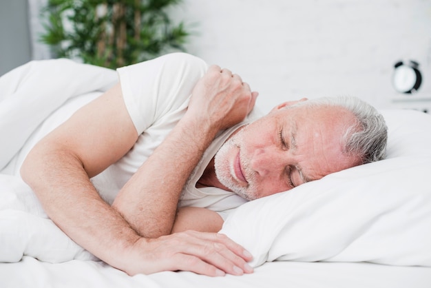 Foto l'anziano uomo che dorme in un letto bianco