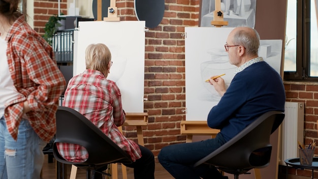 Gli anziani imparano a disegnare su tela nel laboratorio d'arte presso il centro comunitario, frequentando la classe per lo sviluppo e la crescita personale. lezione di disegno e pratica con strumenti artistici. scatto da treppiede