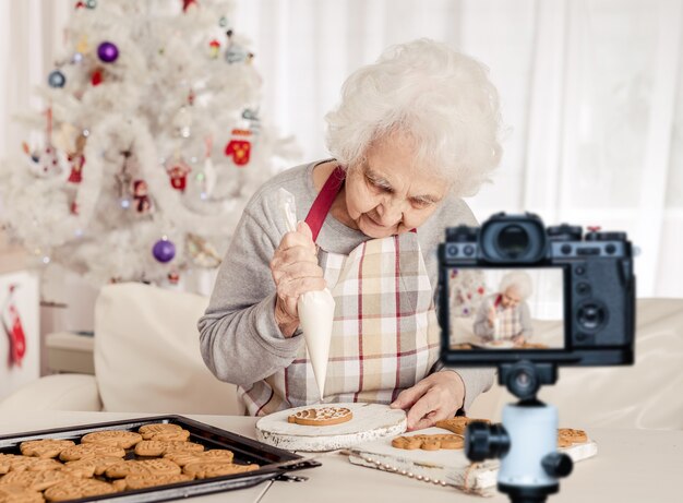 クリスマスの焼きたてのクッキーにクリームを浸す年配の女性