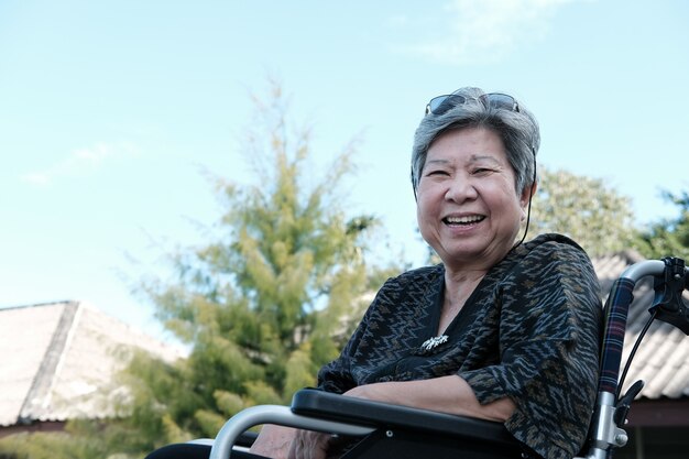 Elder woman on wheelchair smiling & resting in garden. 