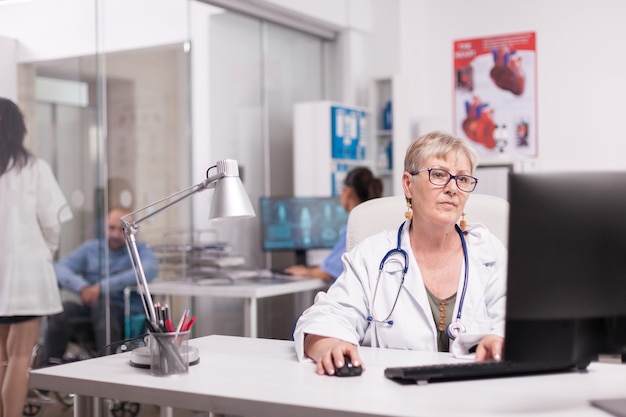 Photo elderly aged woman doctor working on pc in hospital office, young therapist discussing with invalid patient in wheelchair and nurse looking at x-ray on computer screen.