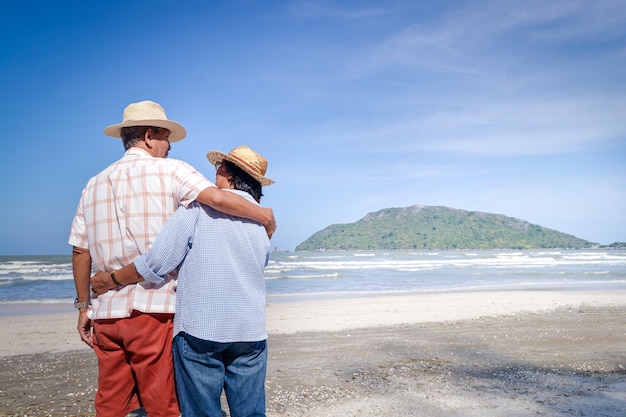 An elderly Asian couple hugging each other on the beach