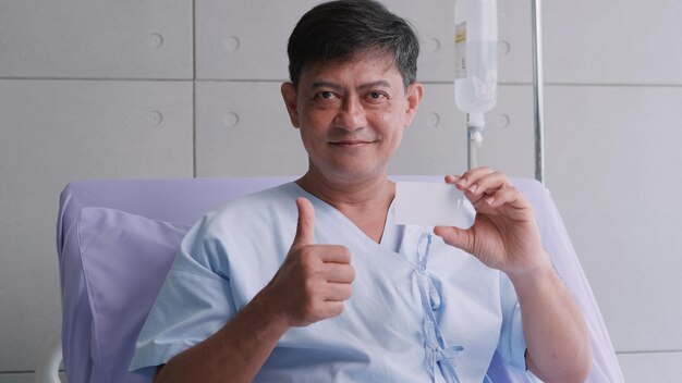 Elderly Asian male patient holding life insurance card during hospitalization