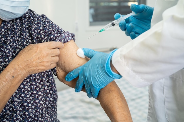 Elderly Asian senior woman wearing face mask getting covid 19 or coronavirus vaccine by doctor make injection19 or coronavirus vaccine by doctor make injection