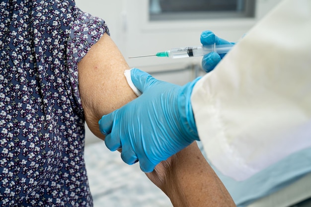 Elderly Asian senior woman wearing face mask getting covid-19 or coronavirus vaccine by doctor make injection.