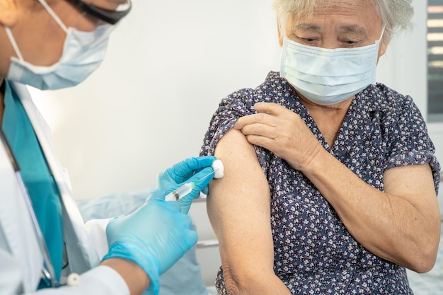 Elderly Asian senior woman wearing face mask getting covid19 or coronavirus vaccine by doctor make injection