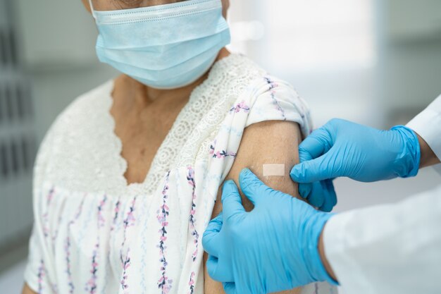 Elderly Asian senior woman wearing face mask getting covid19 or coronavirus vaccine