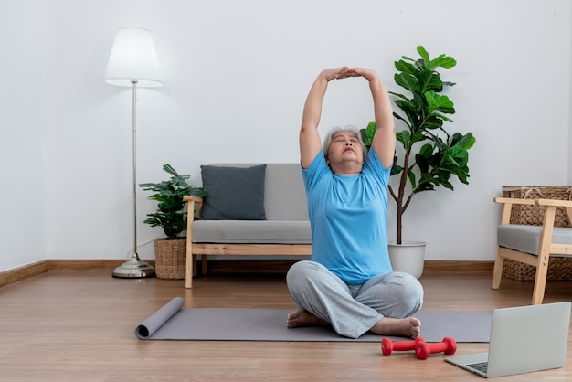 Photo elderly asian woman practicing yoga in basic position in living room