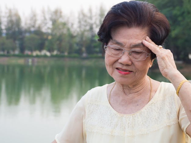 노인 아시아 여성은 안경을 착용했다. 그녀는 두통에 익숙하지 않았다.