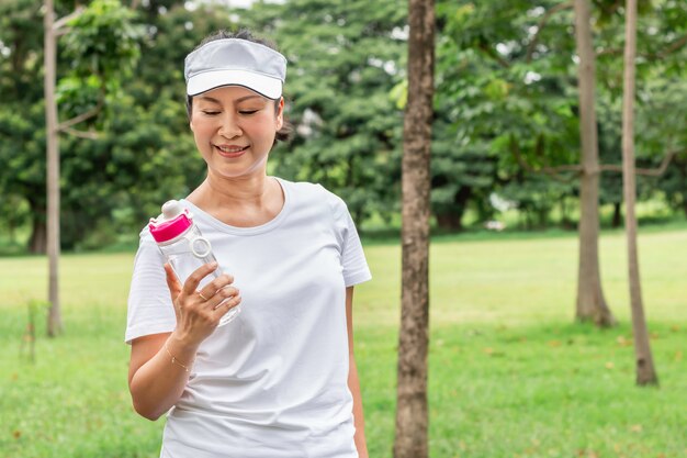 노인 아시아 여성 여름 공원에서 신선한 물을 마시는 웃고.