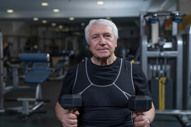 Un atleta anziano in palestra si siede con i manubri in mano