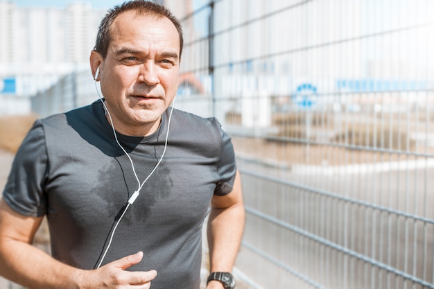 An elderly athlete runs on the street. The mature man is running.