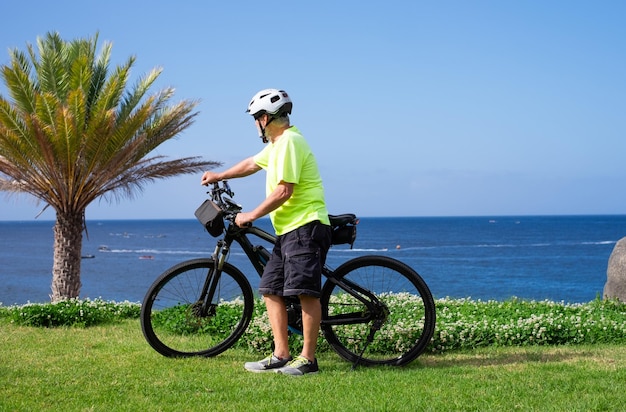 Elderly athletic man with electric bicycle in outdoors excursion at sea enjoying freedom