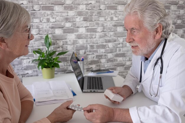 Elderly bearded male doctor and female patient meeting at\
annual checkup visit checking therapy healthcare and medicine\
concept