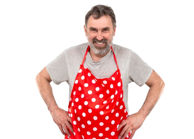 An elderly bearded man in a red polkadot culinary apron on a white background