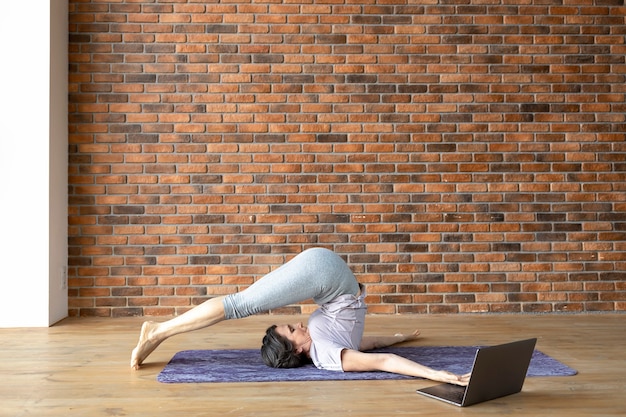 Elderly beautiful athletic woman using laptop doing yoga or fitness online