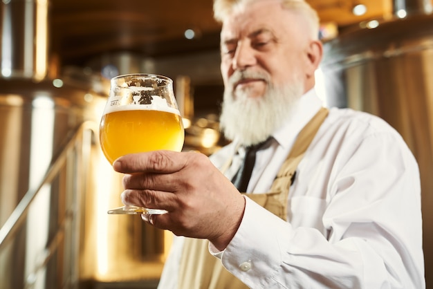 Elderly brewer holding glass with light beer