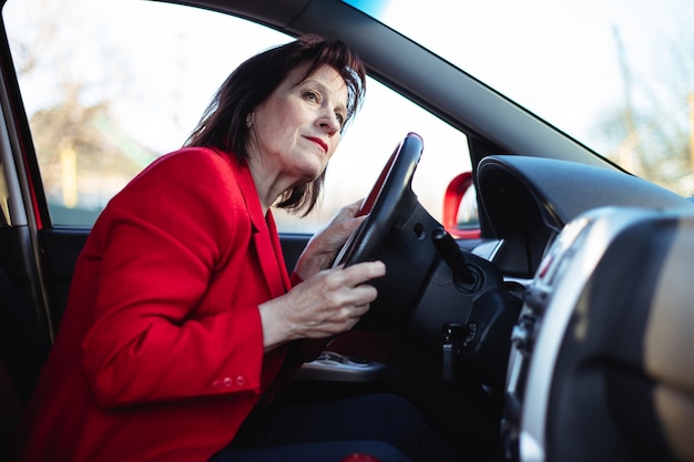 노인 비즈니스 여성이 그녀의 차를 운전하고 있습니다. 주요 도로에서 엿보기