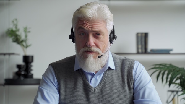 An elderly businessman in a headset having a video conference with a business partner working in an office