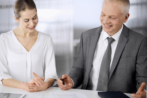 Elderly businessman and woman sitting and communicating in office. Adult business people or lawyers working together as a partners and colleagues at meeting. Teamwork and cooperation concept.