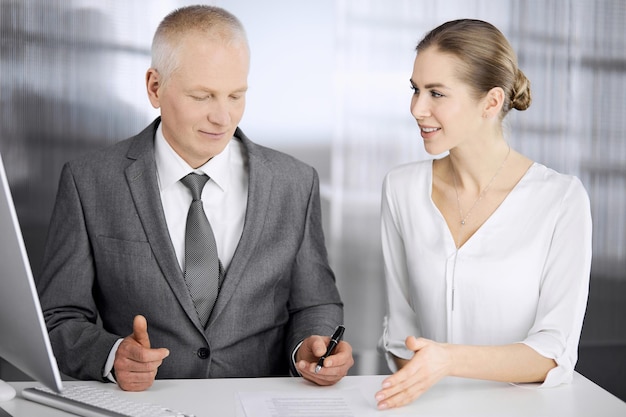 Elderly businessman and woman sitting and communicating in office. Adult business people or lawyers working together as a partners and colleagues at meeting. Teamwork and cooperation concept.