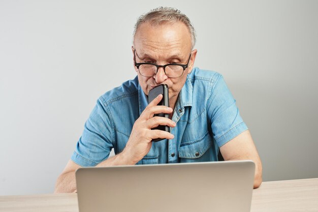 Elderly Caucasian man in glasses with a serious expression on his face working on a laptop at his desk on a white background