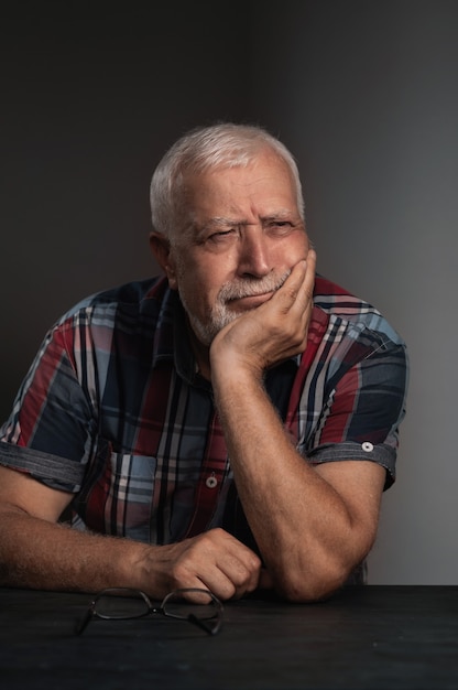 Photo elderly charismatic man in a checkered shirt, frowning with his head on his hand, close-up portrait on a gray background