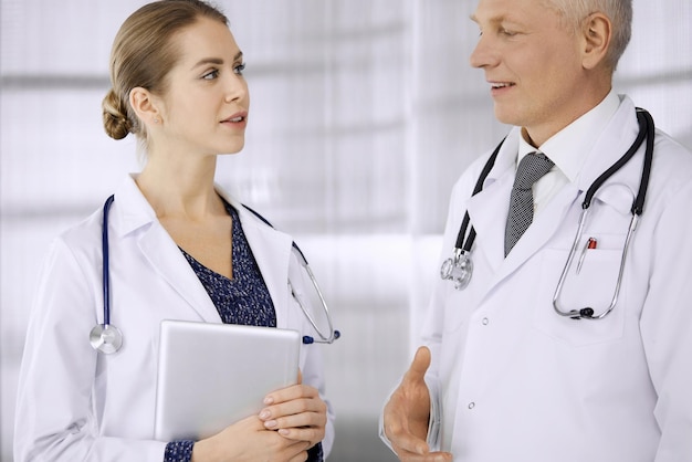 Elderly confident doctor and woman physician discussing current disease therapy while standing in clinic Teamwork in hospital Medicine and healthcare concept