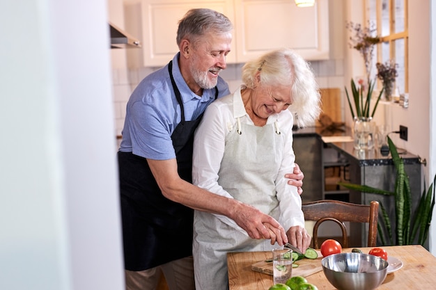 Elderly couple carving vegetables together, handsomegray haired man help wife to cook