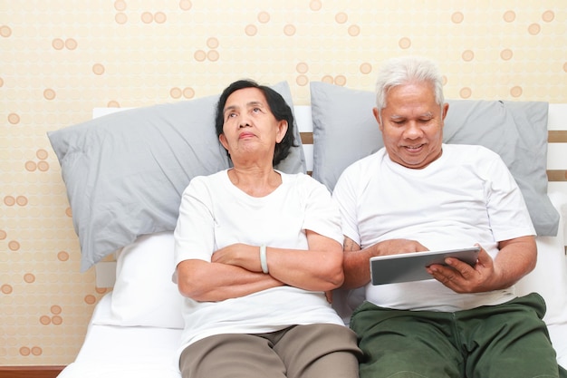 Elderly couple lying in bed Wife dissatisfied with husband playing tablet Family concepts health care for the elderly retirement age