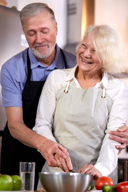Пожилая пара готовит овощной салат на кухне, седой красавец помогает жене с приготовлением пищи, собираясь на здоровый завтрак. сосредоточиться на руках