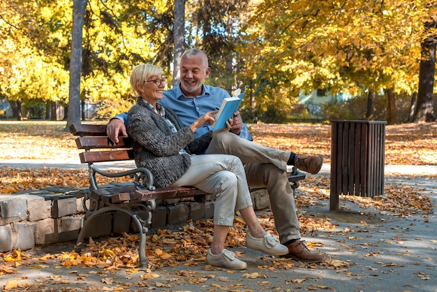 Фото Пожилая пара сидит на скамейке и читает книгу в парке