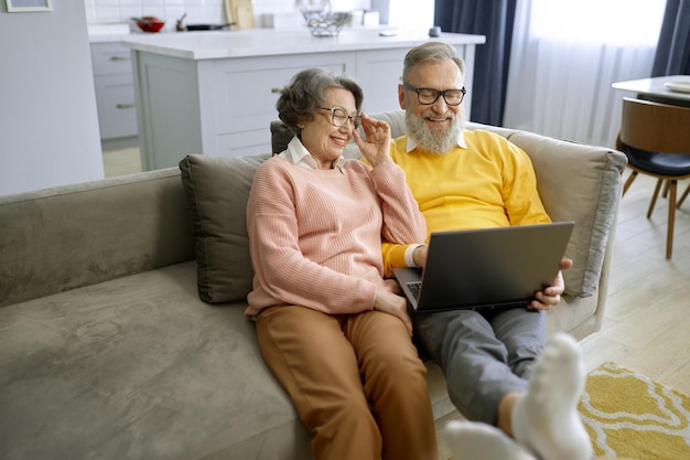 Elderly couple using laptop together and sitting on couch at home