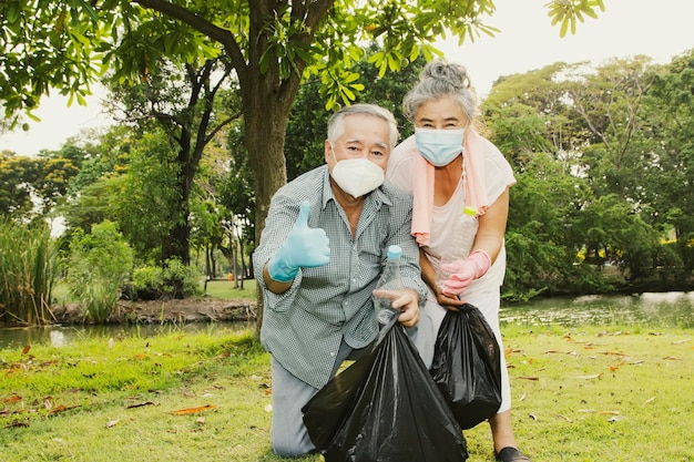 Пожилая пара добровольно собирает пластиковые бутылки в черные пакеты, чтобы содержать сад в чистоте.