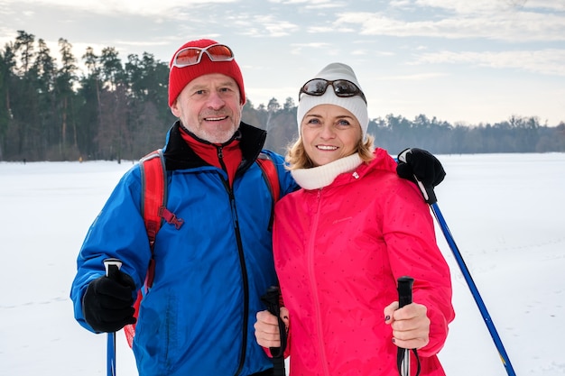 Coppie anziane che camminano con i bastoncini da nordic walking in snowy winter park