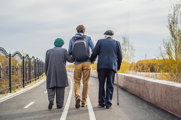 An elderly couple walks in the park with a male assistant or adult grandson. Caring for the elderly, volunteering