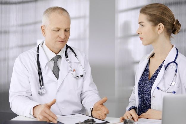 Elderly doctor and his female colleague discussing current disease therapy while sitting at working place in clinic Teamwork in hospital Medicine and healthcare concept