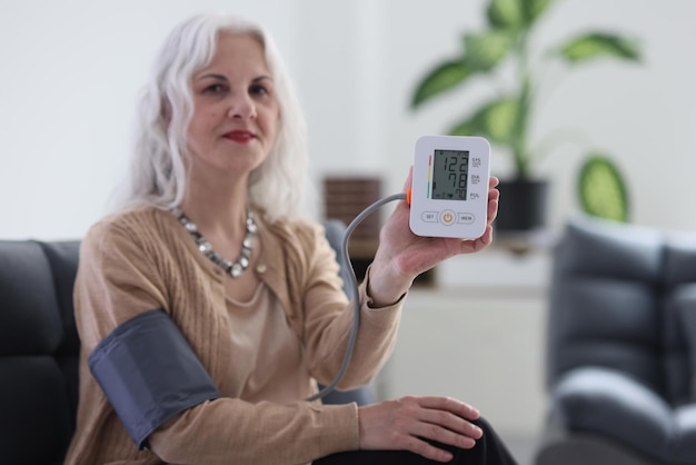 Elderly greyhaired woman with long grey hair measures blood pressure using digital tonometer