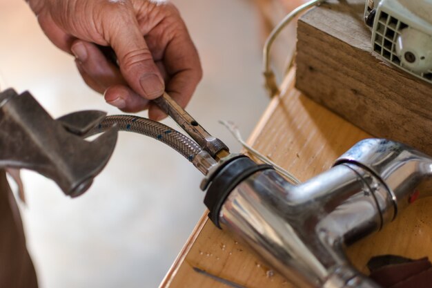 Elderly hands fixing the water tap with spanner, close up.