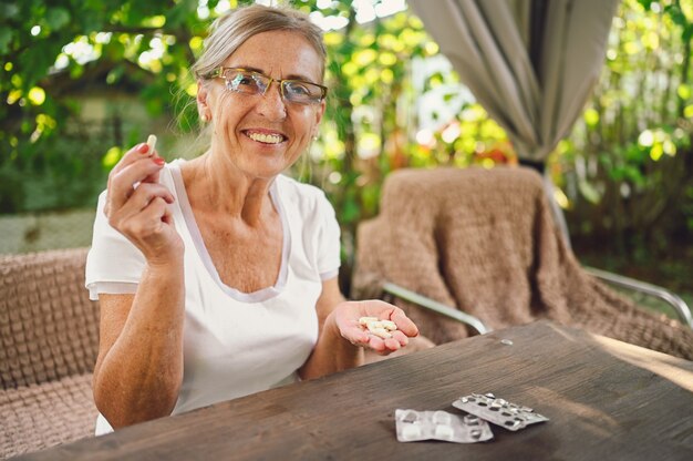 Photo elderly happy senior old woman in spectacles prescription glasses takes medicine drugs vitamins pills outdoors in the garden. healthcare aged people lifestyle concept